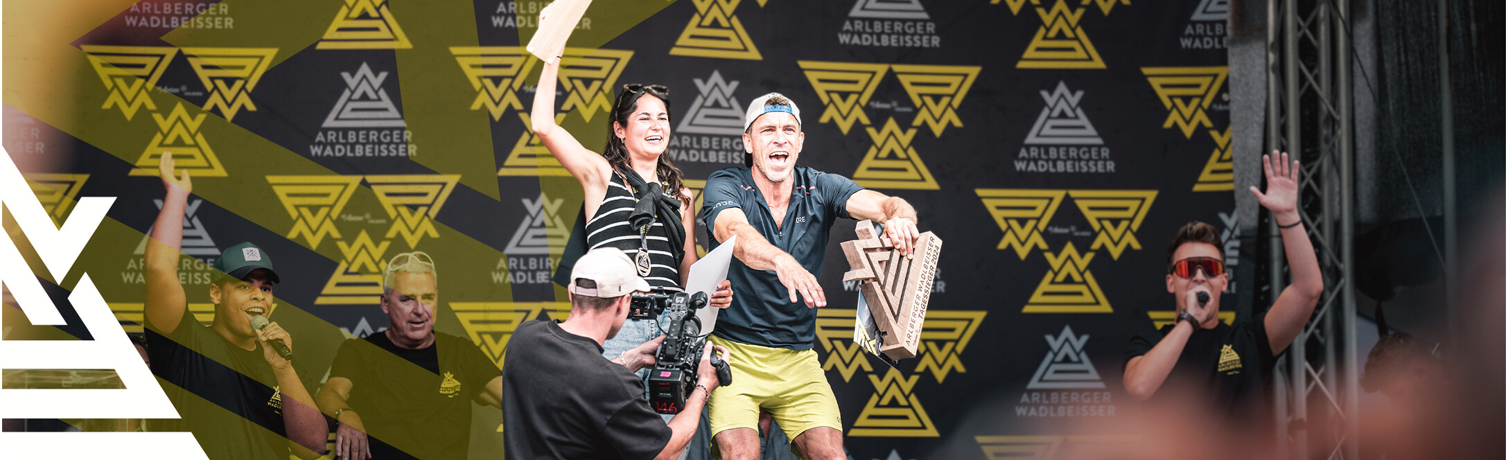 Siegerin und Sieger des Arlberger Wadlbeisser 2024 auf der Bühne nach der Preisvergabe. Arlberger Wadlbeisser Logo als Designelemnt in weiß am linken Bildrand.