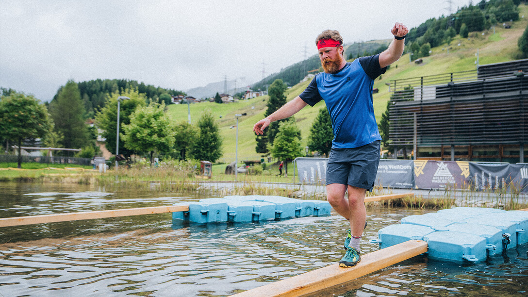 Sportler balanciert über einen Balken, welcher in einem Teich schwimmt / Athlete balances on a beam floating in a pond 