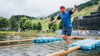 Sportler balanciert über einen Balken, welcher in einem Teich schwimmt / Athlete balances on a beam floating in a pond 