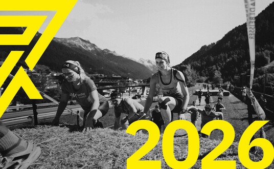 Athletinnen bezwingen das Hinernis "Heureka". "2026" steht in gelb unten rechts geschrieben. Arlberger Wadlbeisser Logo ist als Designelement oben links zu sehen. 